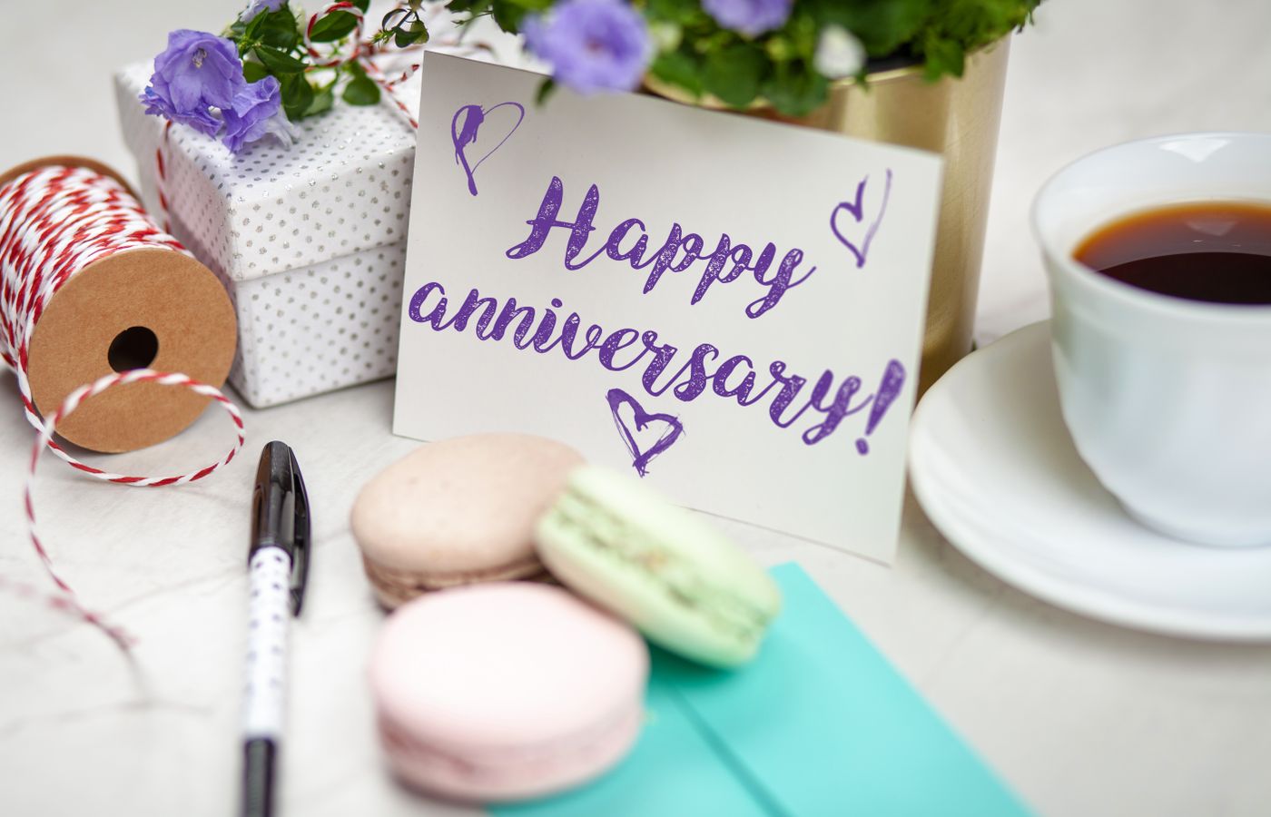 Happy anniversary card with flowers, gift, macarons, and coffee on a table.