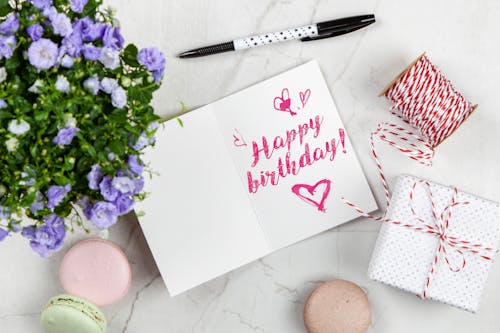 Free Открытка с днем рождения рядом с цветком, ниткой, коробкой и миндальным печеньем Stock Photo