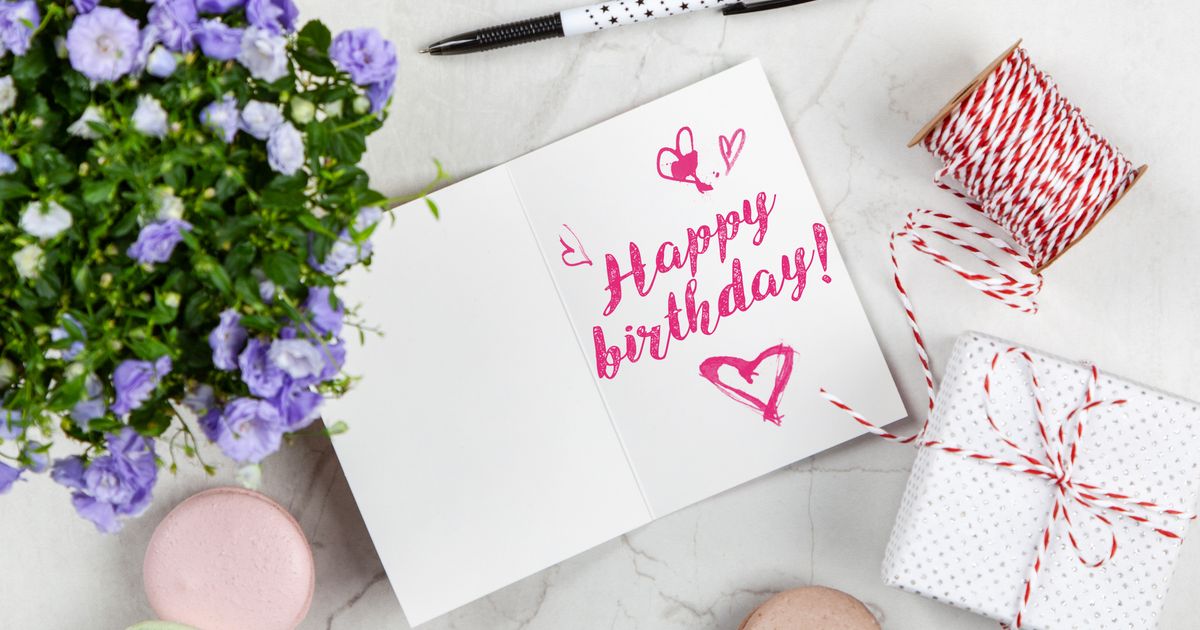 Birthday card with purple flowers, a wrapped gift, and macarons on a marble surface