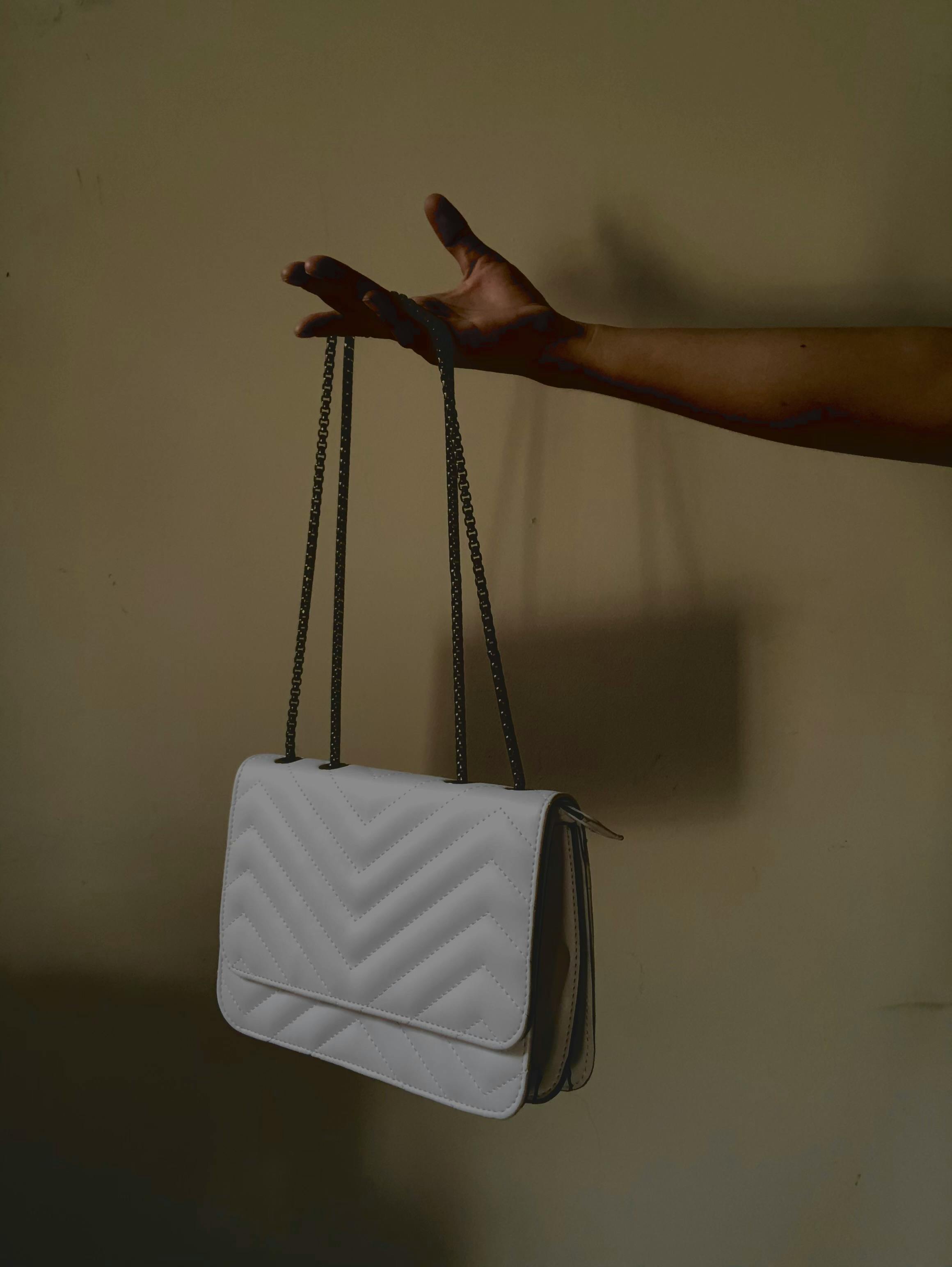 Free A minimalist photo of a white quilted bag gracefully held by a woman's hand, showcasing fashion elegance. Stock Photo