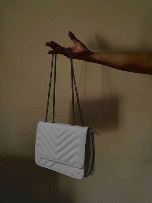 Free A minimalist photo of a white quilted bag gracefully held by a woman's hand, showcasing fashion elegance. Stock Photo
