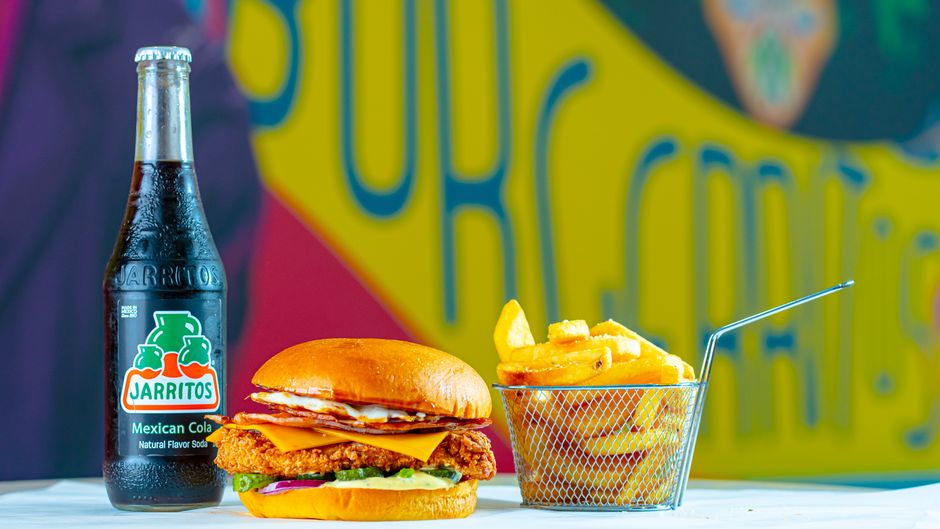Fotomural Una comida rápida y deliciosa que incluye una hamburguesa, papas fritas y Jarritos Cola Mexicana sobre un fondo vibrante.