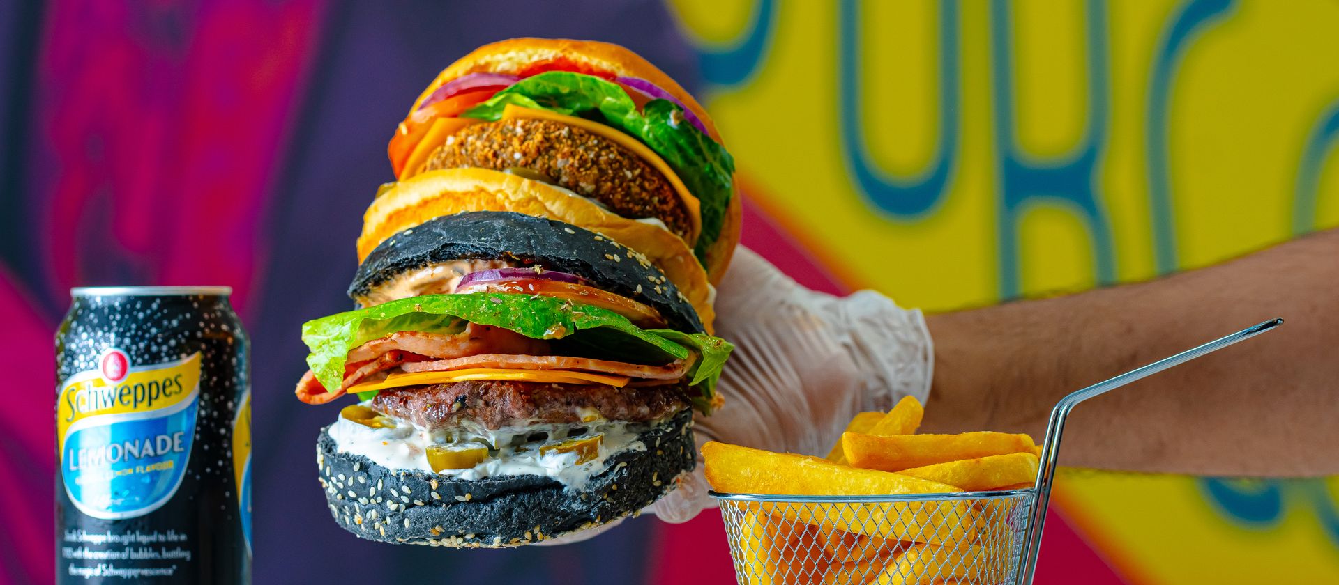 Vibrant image of a gourmet burger with fries and Schweppes lemonade in an artistic setting.