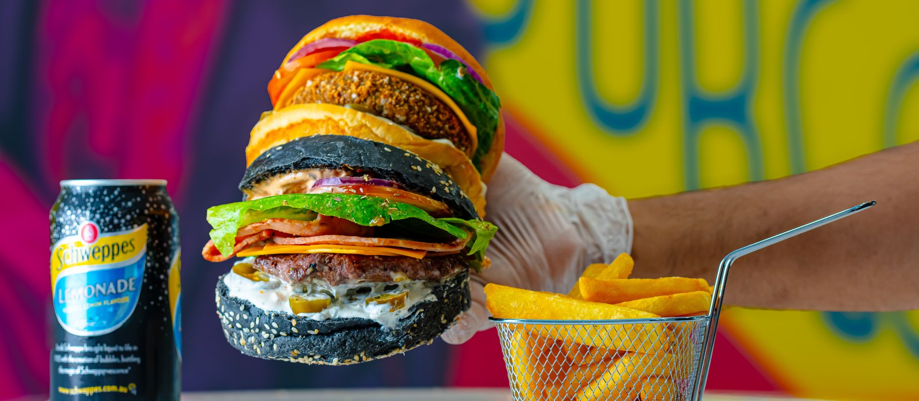 Close-up of gourmet burgers with black buns, served with fries and a lemonade can.