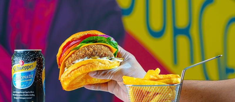 Vibrant image of a gloved hand holding a delicious burger with soda and fries.