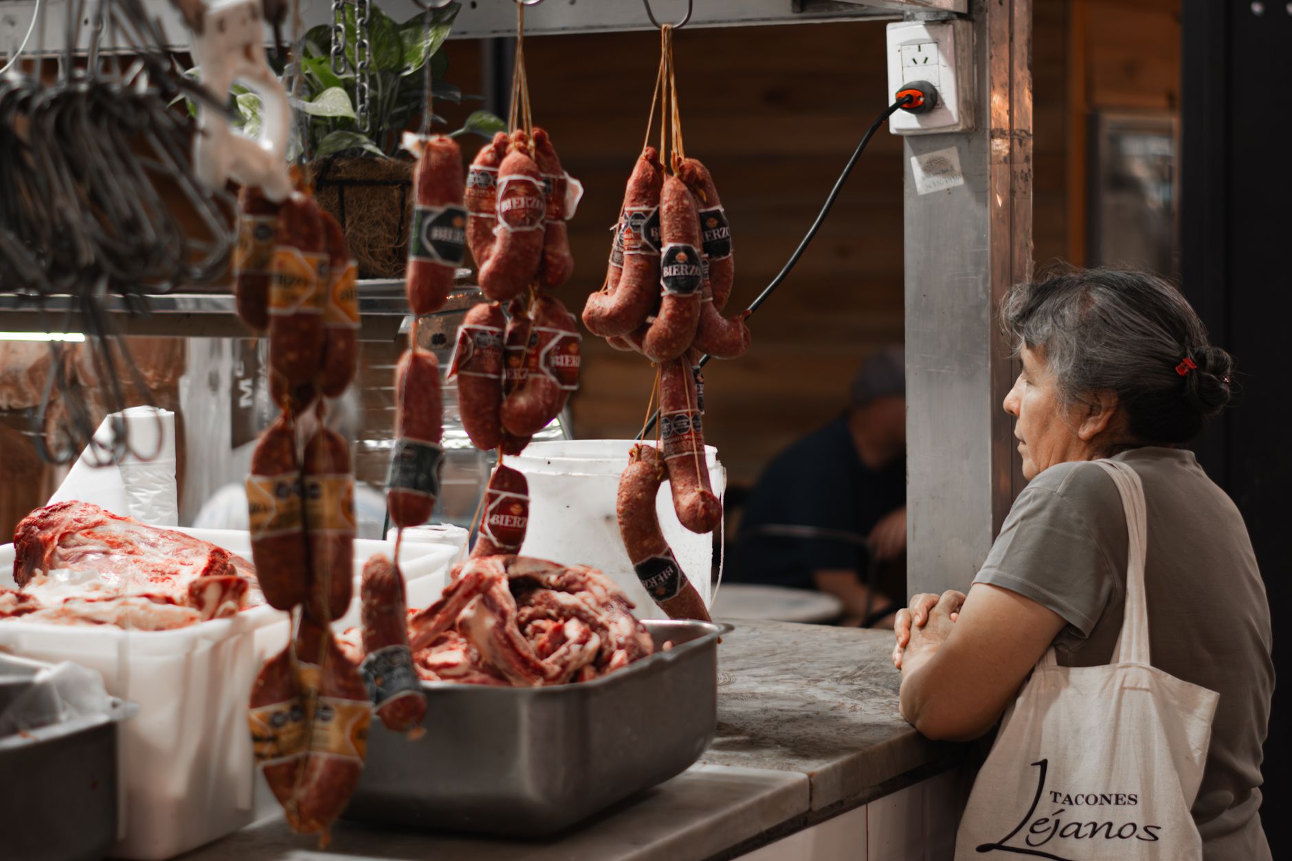 A woman browses hanging sausages and raw meat in a butcher shop