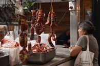 A woman browses hanging sausages and raw meat in an Argentine butcher shop.