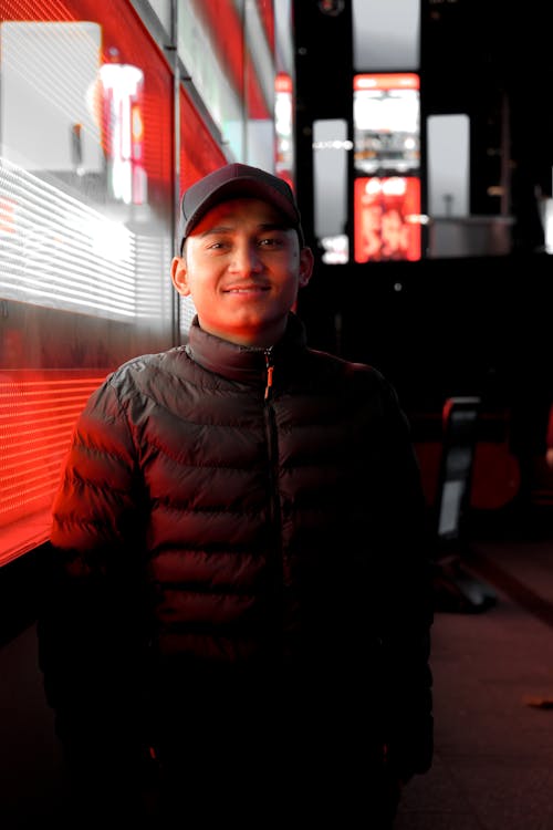 A man in a jacket and hat standing in front of a red wall