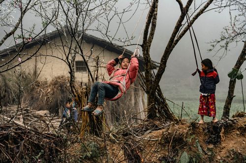 Free Two children enjoy playing on swings in a rural village, showcasing joy and nature. Stock Photo