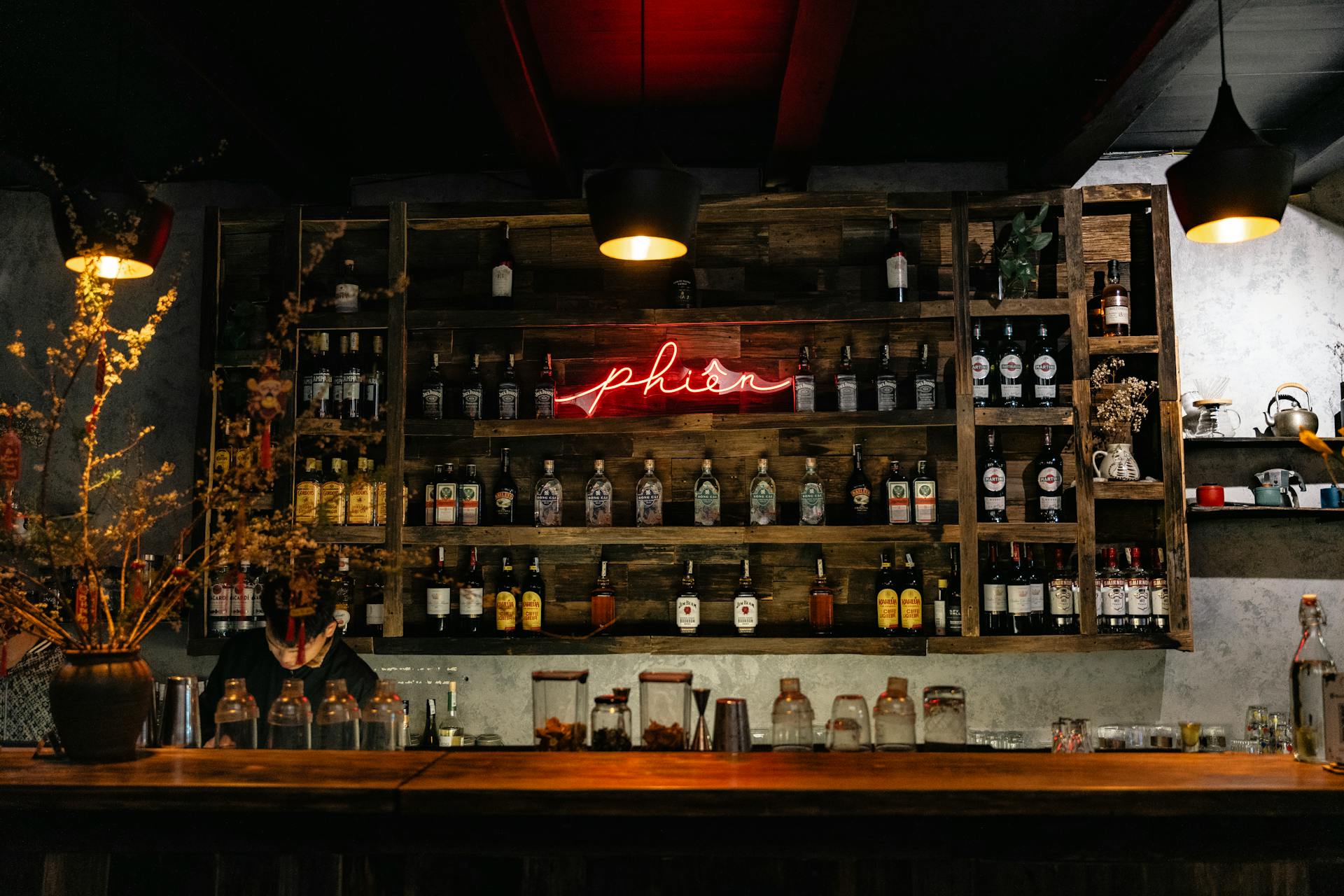 Cozy bar interior with wooden shelves, bottles, and a red neon sign creating a warm ambiance.