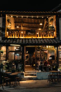 Warmly lit rustic cafe with people seated outside at night, exuding cozy charm.