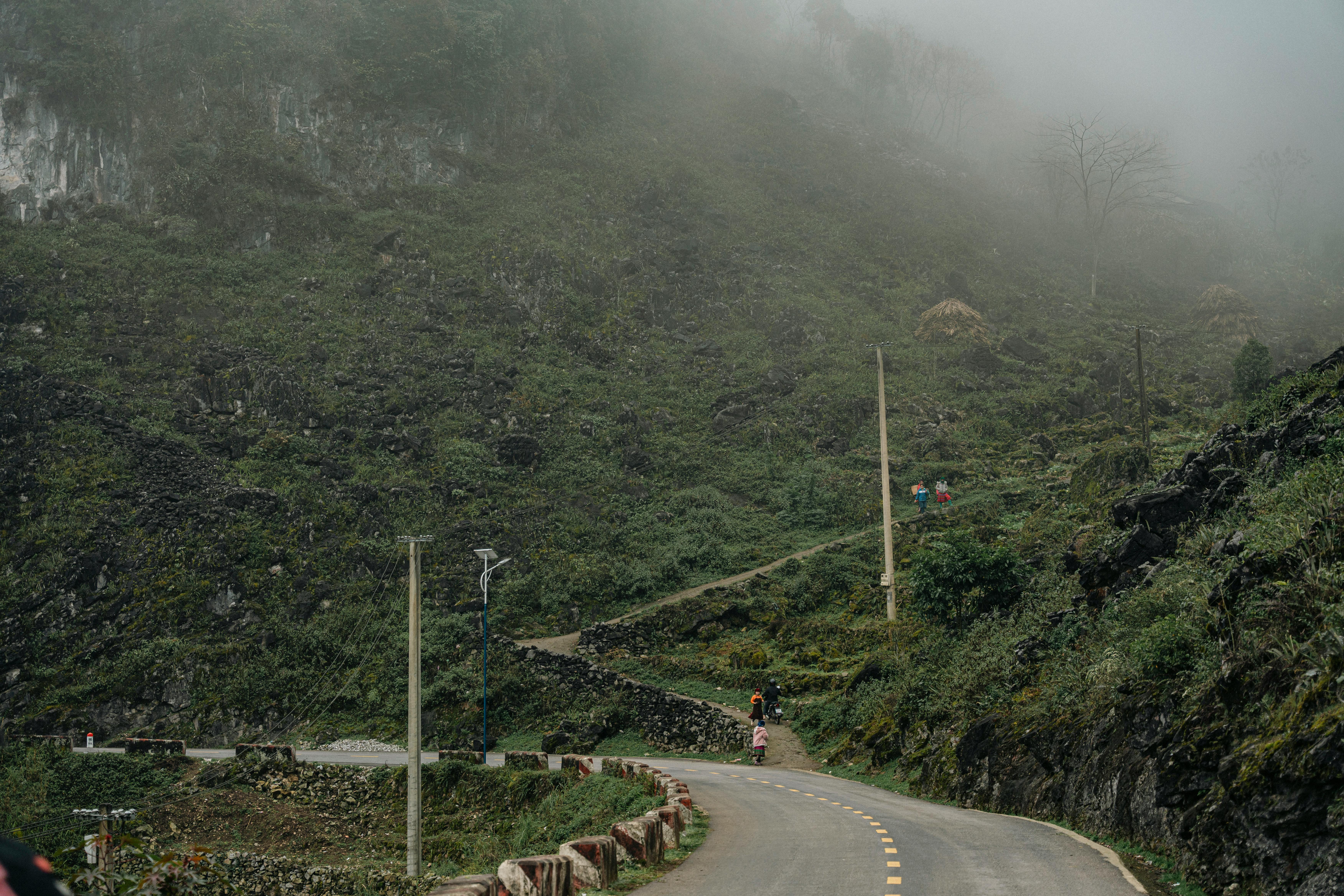 A winding rural road through foggy mountain terrain with lush vegetation and paths.