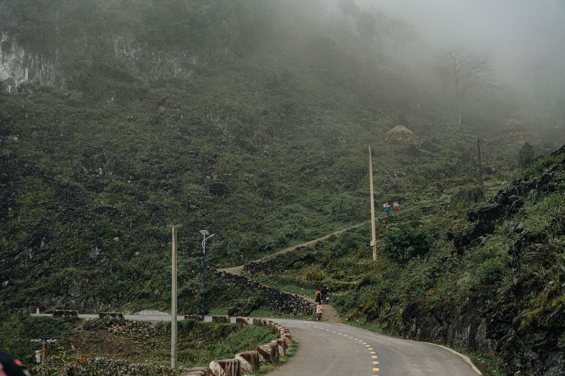 A winding rural road through foggy mountain terrain with lush vegetation and paths.