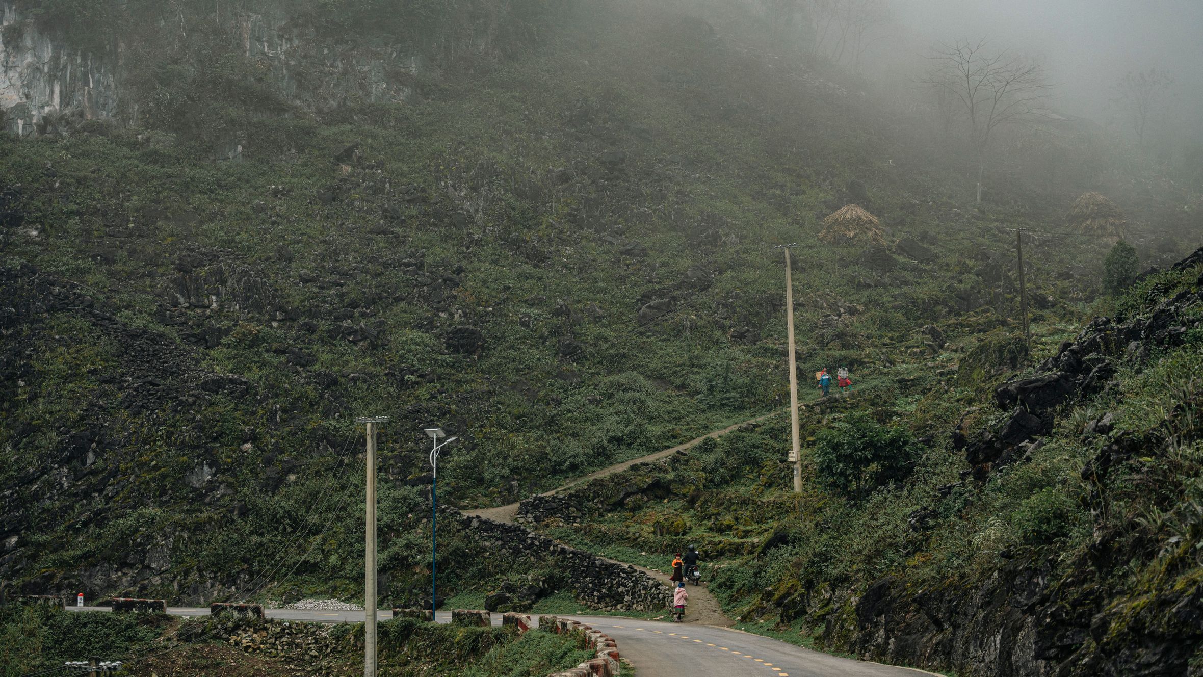A winding rural road through foggy mountain terrain with lush vegetation and paths.