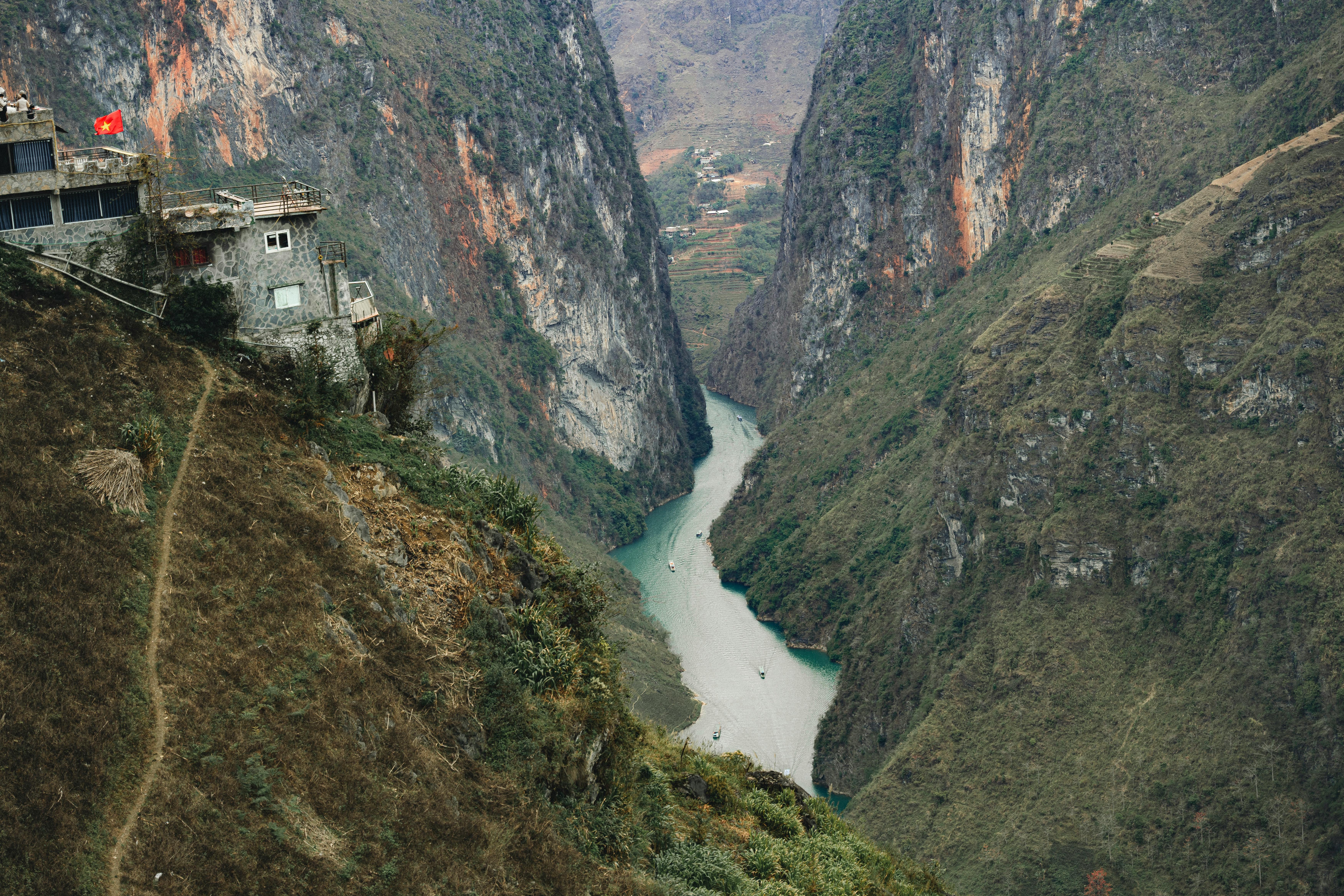 A breathtaking aerial view of a canyon landscape with a river in Vietnam, featuring rugged cliffs and a lone house.