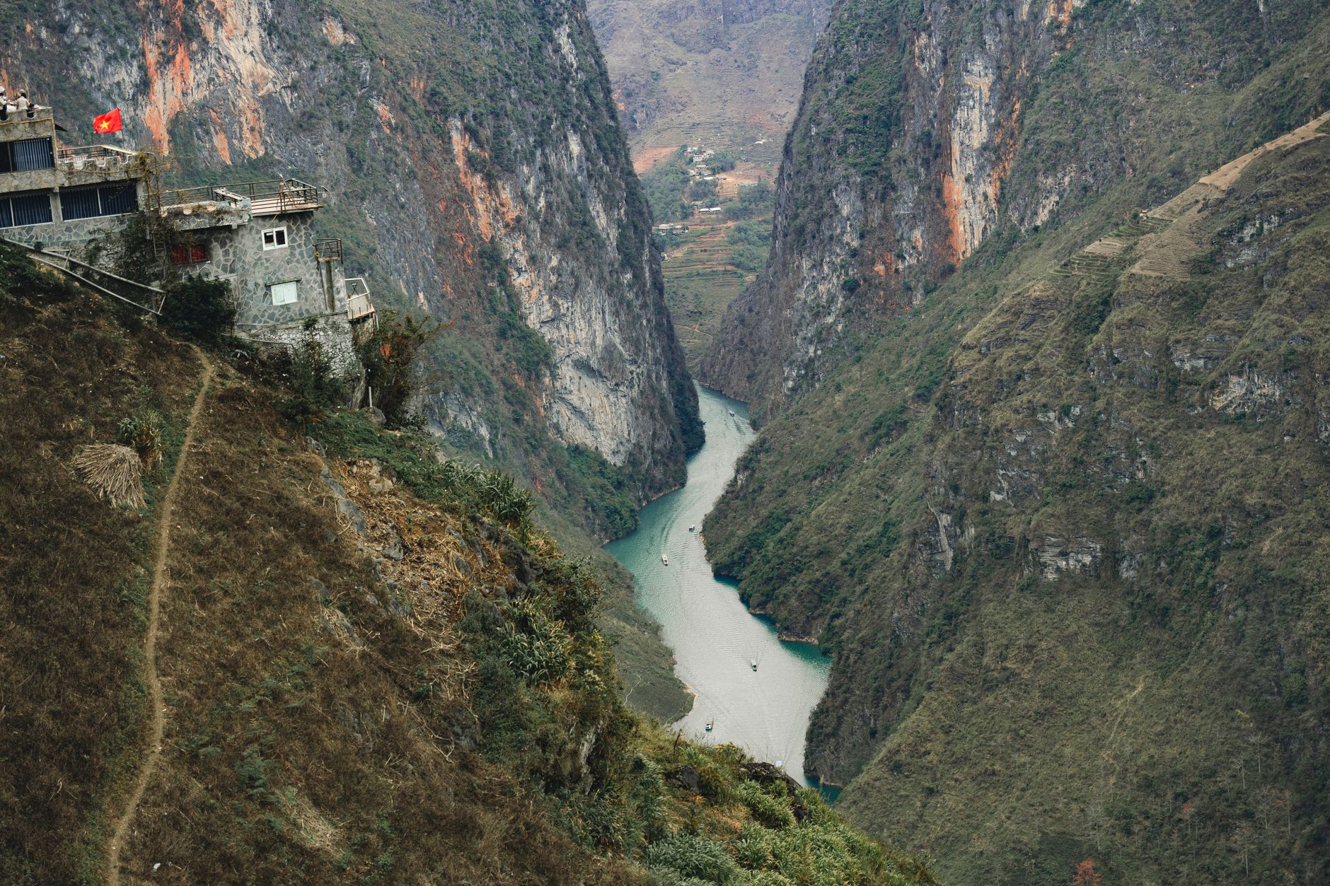 A breathtaking aerial view of a canyon landscape with a river in Vietnam, featuring rugged cliffs and a lone house.