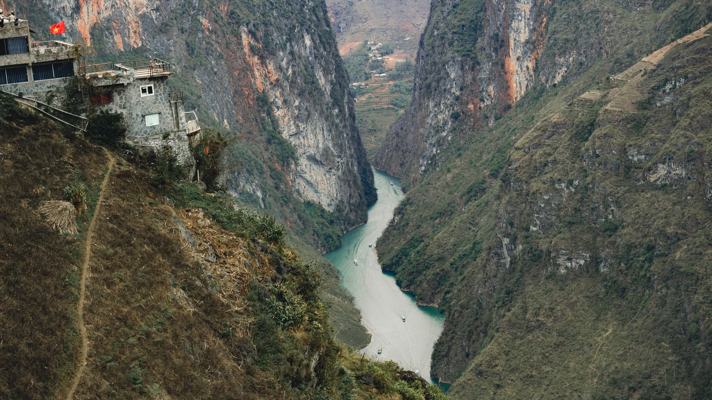 A breathtaking aerial view of a canyon landscape with a river in Vietnam, featuring rugged cliffs and a lone house.