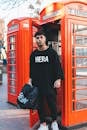 一位穿着街头服饰的时尚男模特在伦敦标志性的红色电话亭前摆姿势