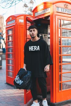 一位穿着街头服饰的时尚男模特在伦敦标志性的红色电话亭前摆姿势