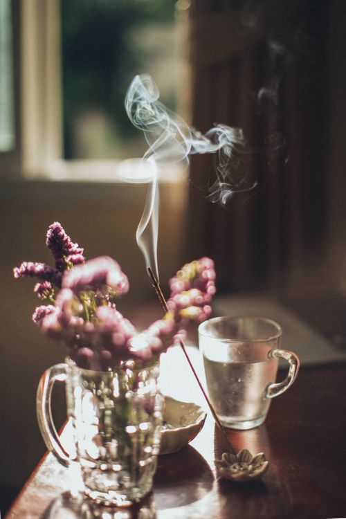 Free Cozy indoor scene with smoke rising above flowers in a glass vase beside a steaming cup. Stock Photo