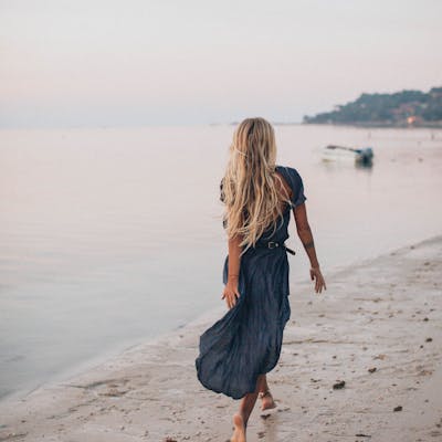 A woman with long hair walks along the beach, enjoying the sun and waves.