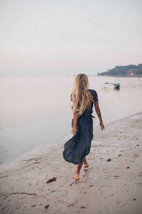 Free Back View of a Woman Walking on the Seashore Stock Photo