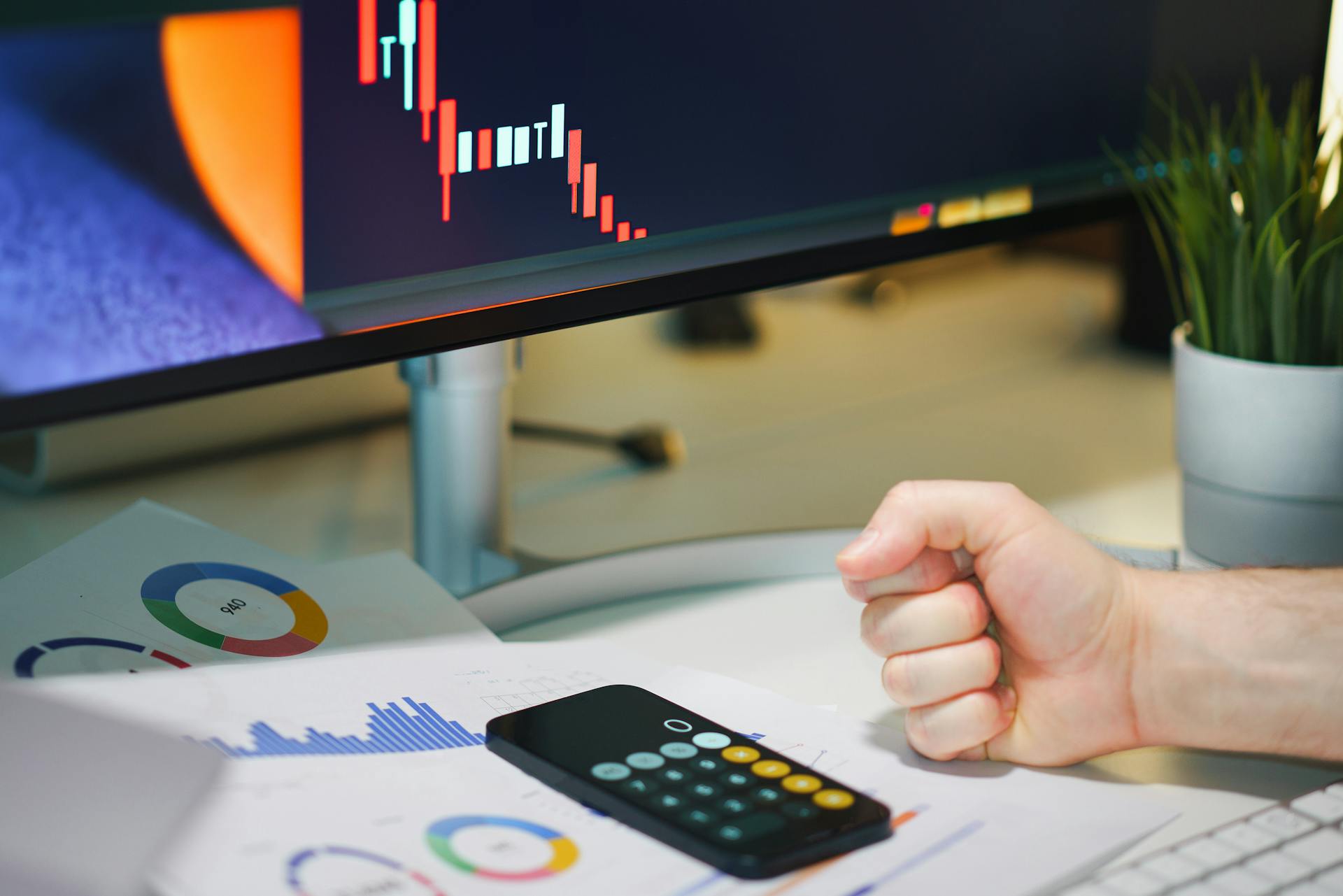 Close-up of a desk with financial graphs, a calculator, and a fist symbolizing determination.