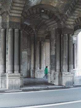 A child walks through a historic walkway under grand stone columns, embodying urban serenity.