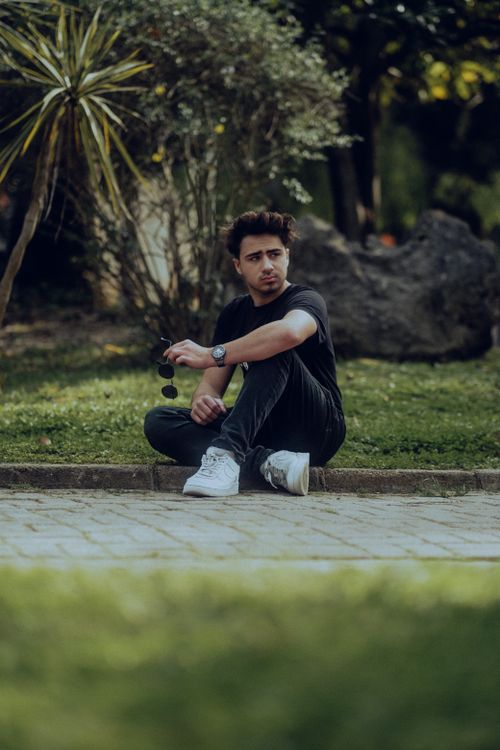 Free Young man in casual attire sitting on a sidewalk in an urban setting. Stock Photo