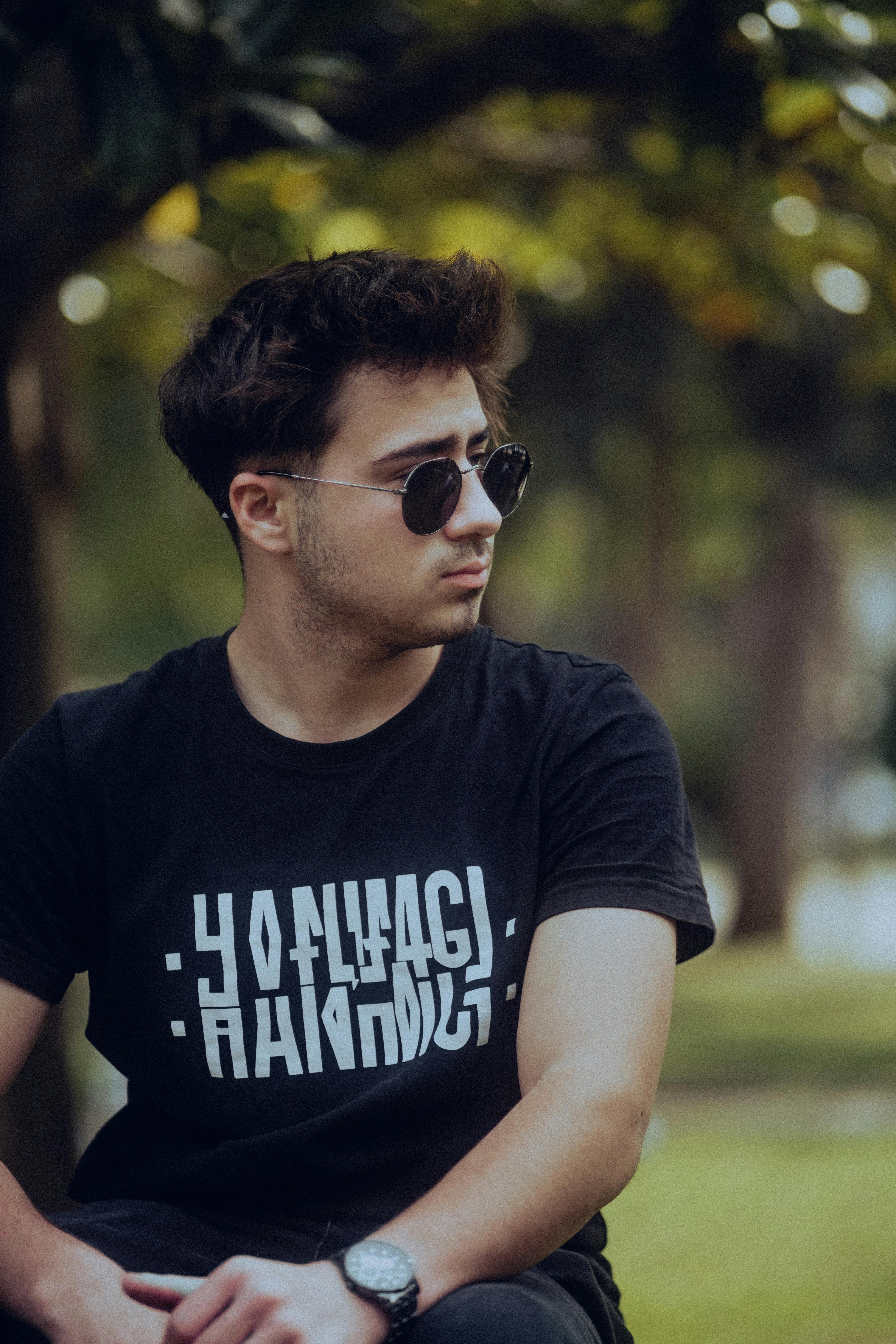 Young man wearing sunglasses and black t-shirt enjoys a sunny day in the park.