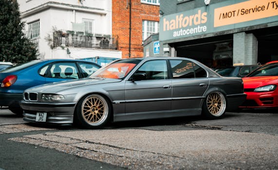 A classic grey BMW E38 sedan parked in front of an urban auto center in Southampton, England.