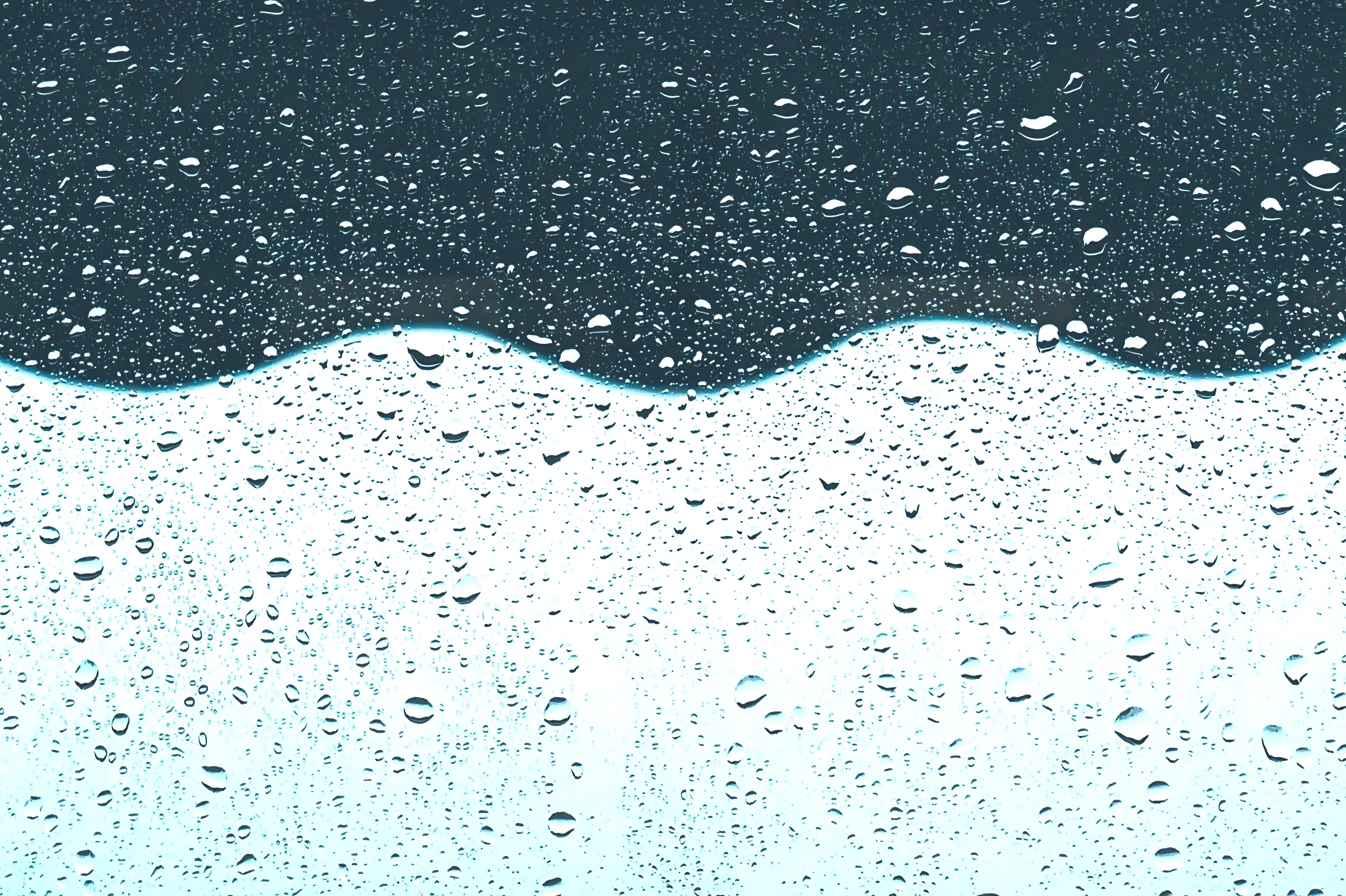 Abstract image capturing raindrops on glass with wavy, reflective surfaces.