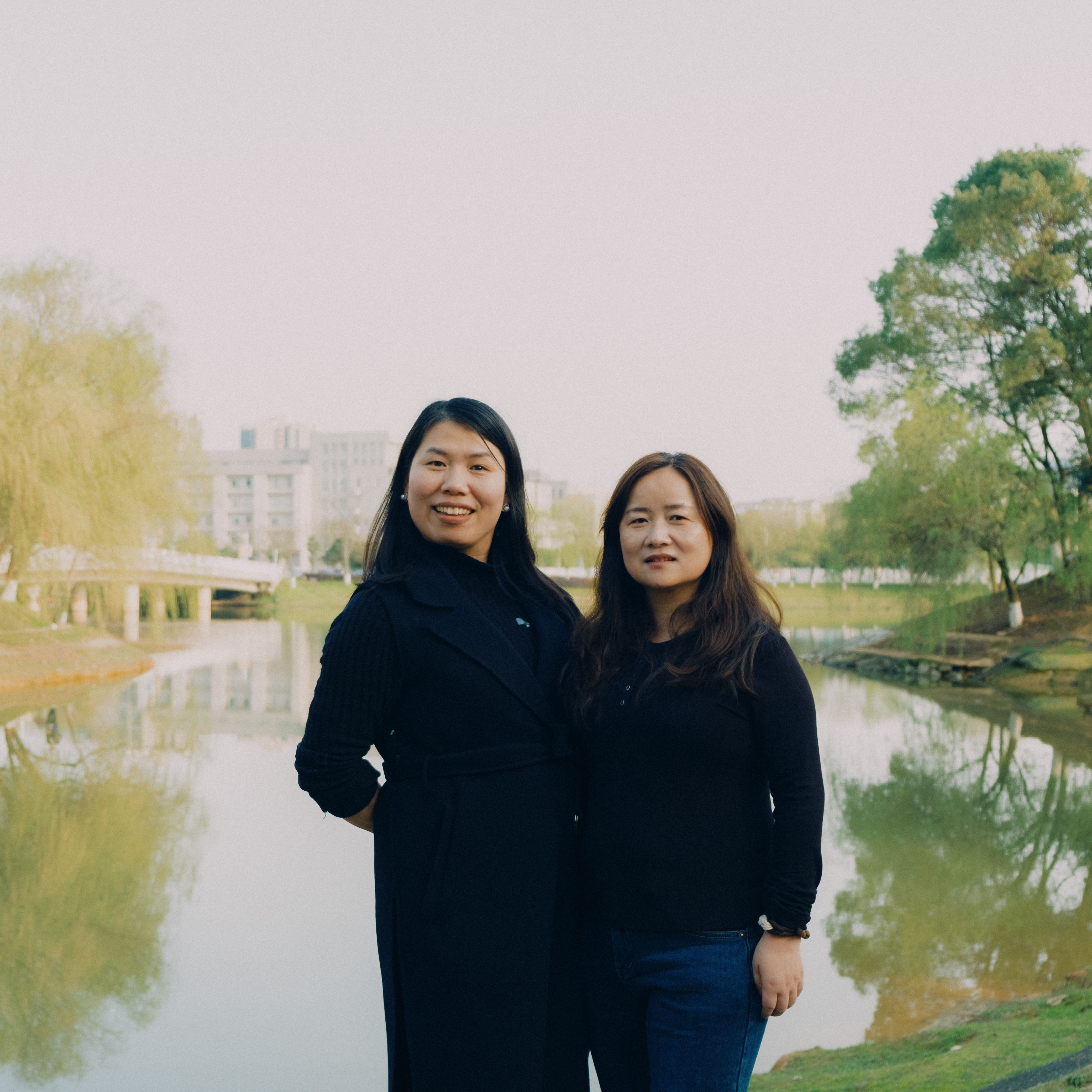 Two women standing by a pond in an urban park, enjoying a sunny day.