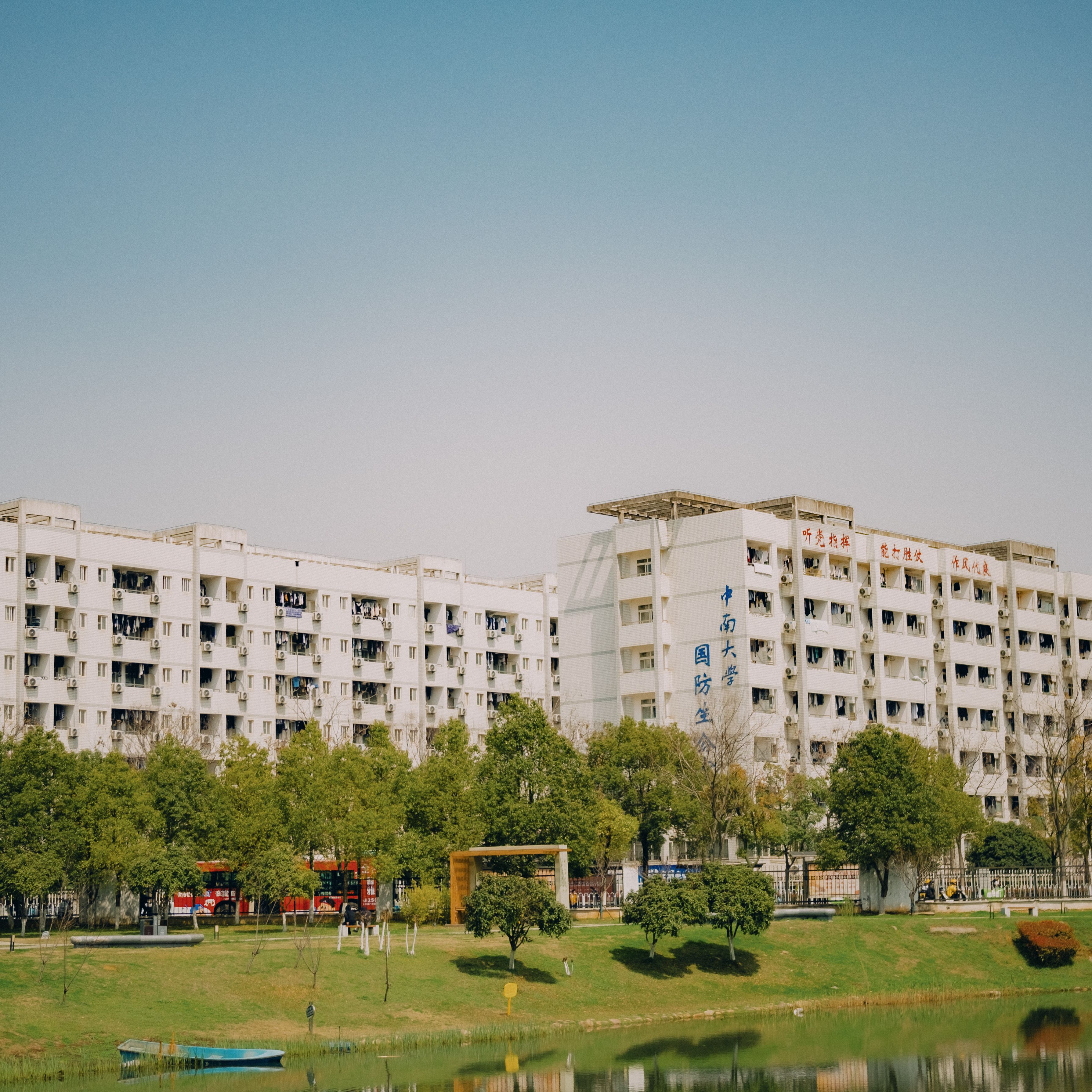 A row of modern apartment buildings overlooking a tranquil park with a pond and trees.