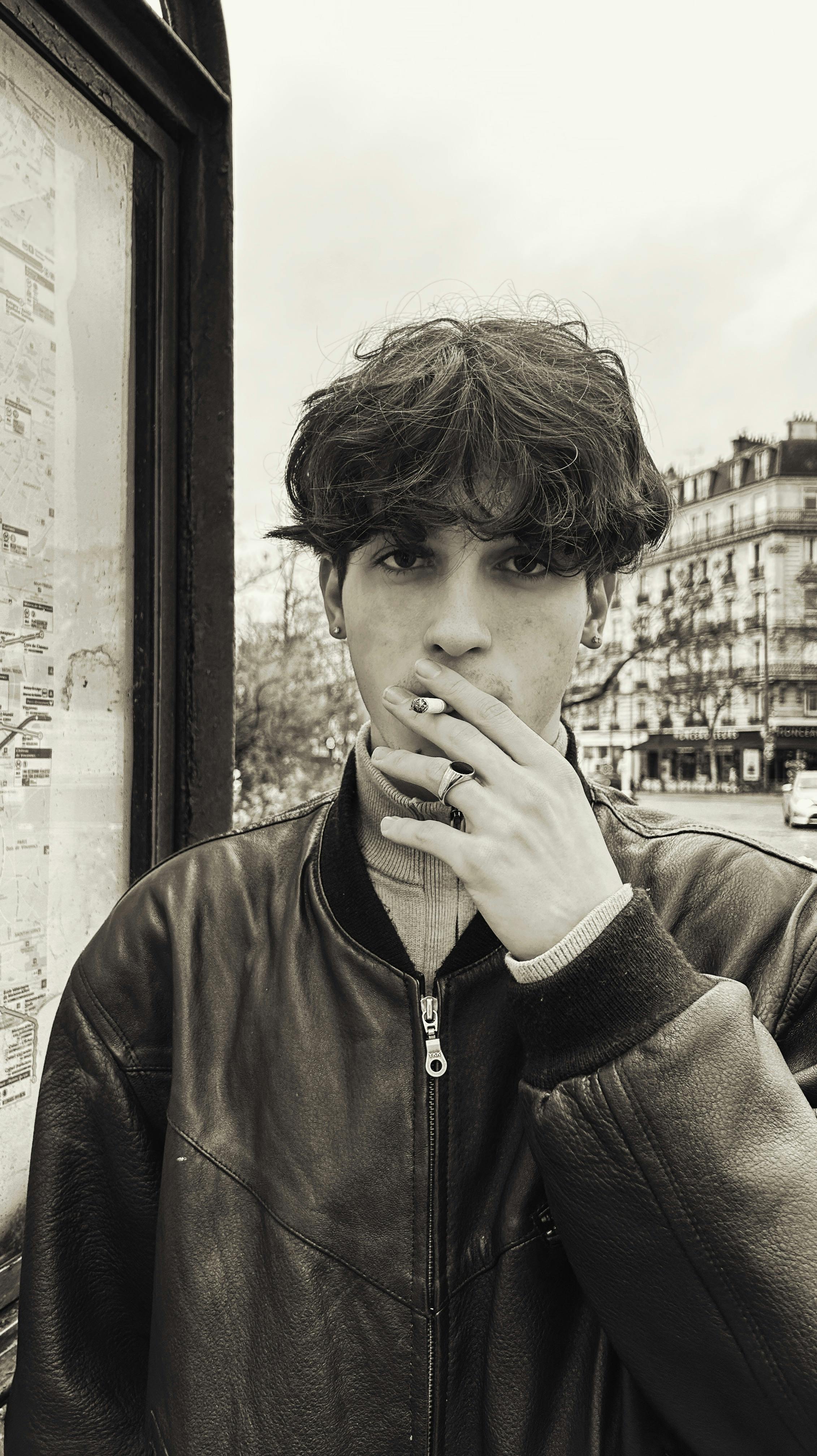 Young man with a leather jacket smoking in the streets of Paris. Urban fashion vibe.