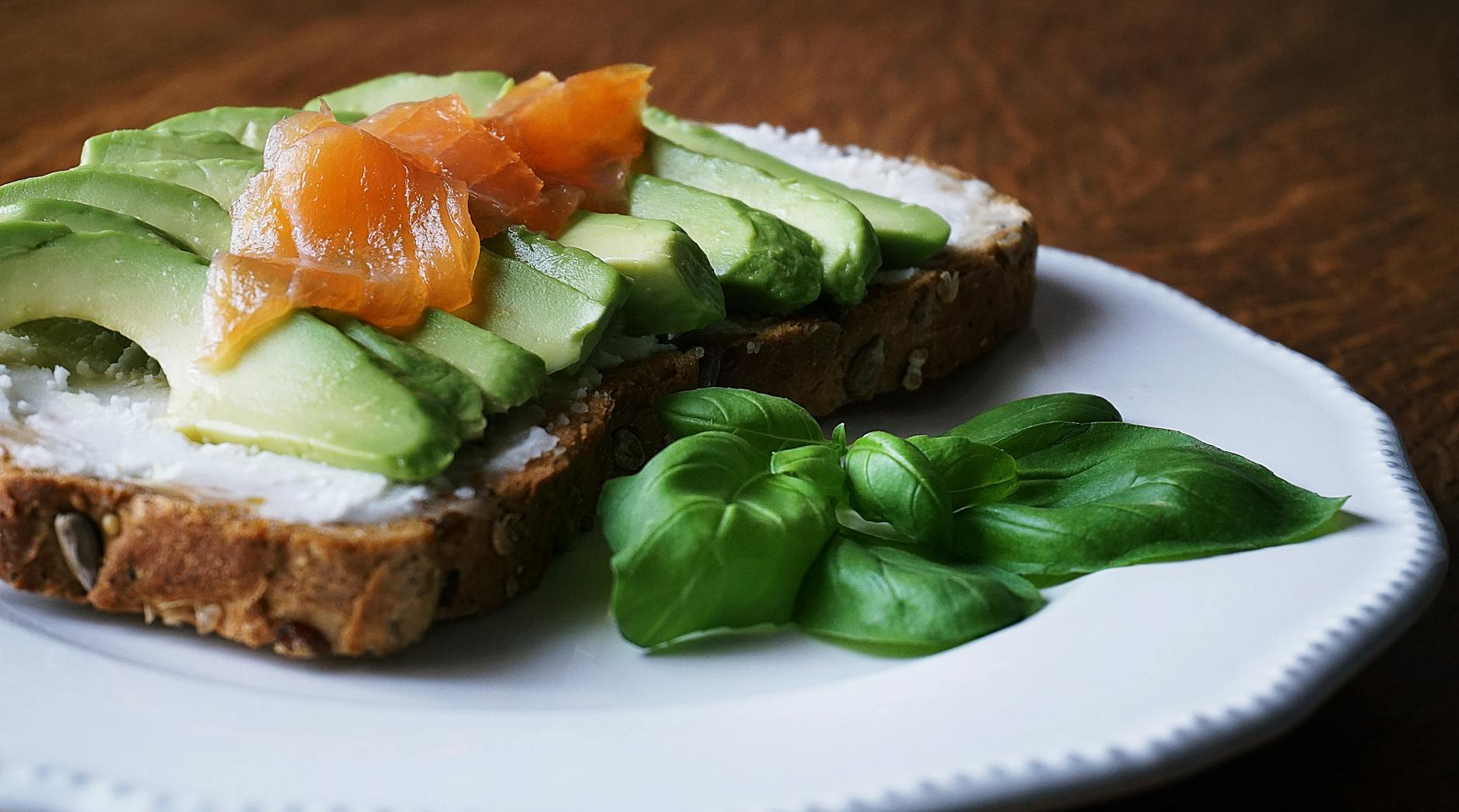 A delicious, healthy meal with avocado and smoked salmon on seeded bread, garnished with basil leaves.