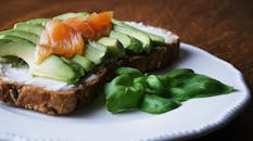 一顿美味健康的饭菜，以鳄梨和烟熏鲑鱼为配菜，搭配有籽面包，并用罗勒叶点缀
