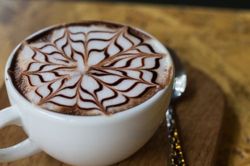 Free Close-up of a cappuccino featuring intricate latte art design on a wooden table. Stock Photo