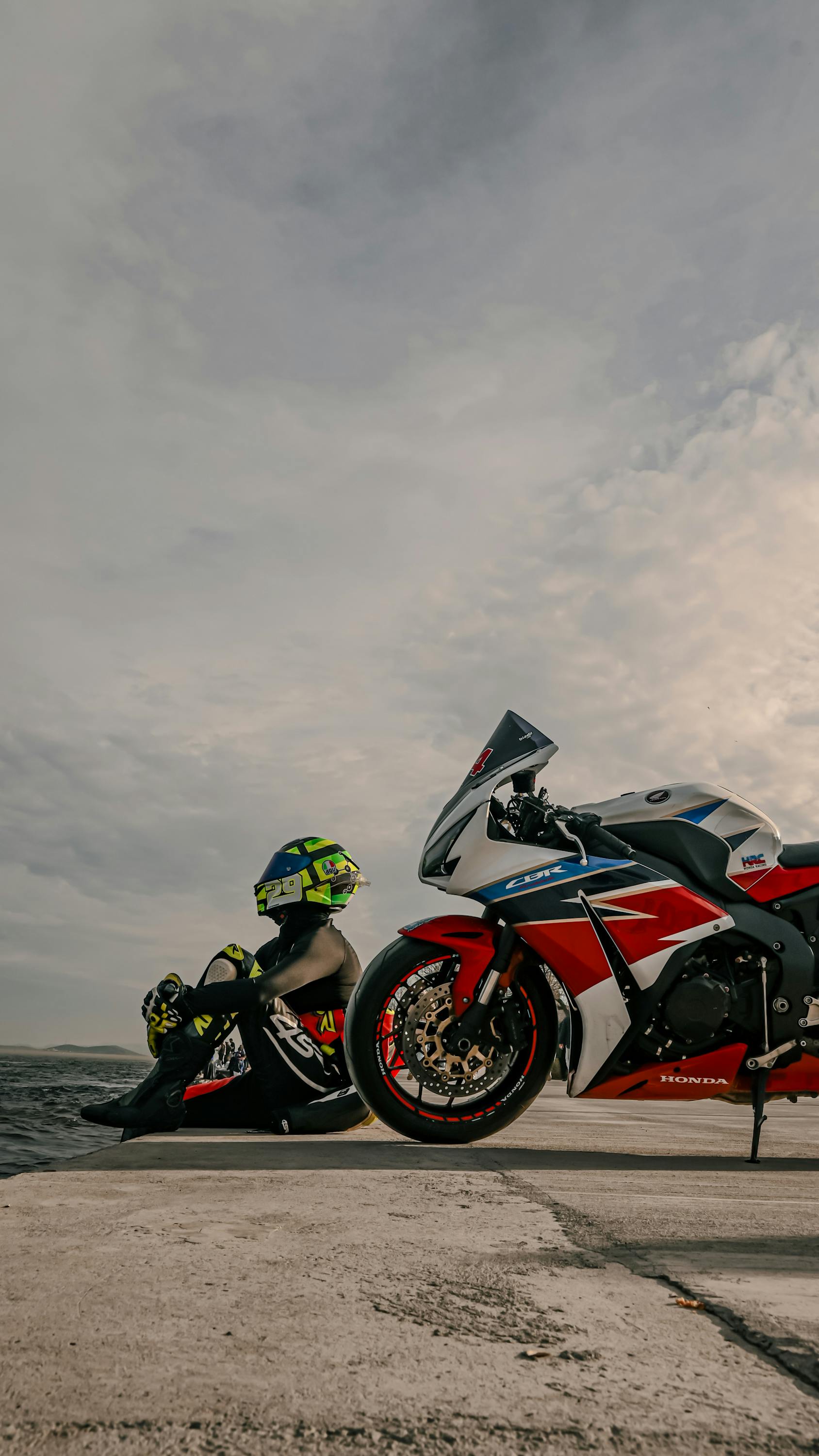 Side view of a person with helmet resting by a Honda motorcycle by the quay.