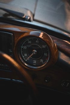 Close-up of a classic car speedometer on a wooden dashboard, evoking vintage elegance.