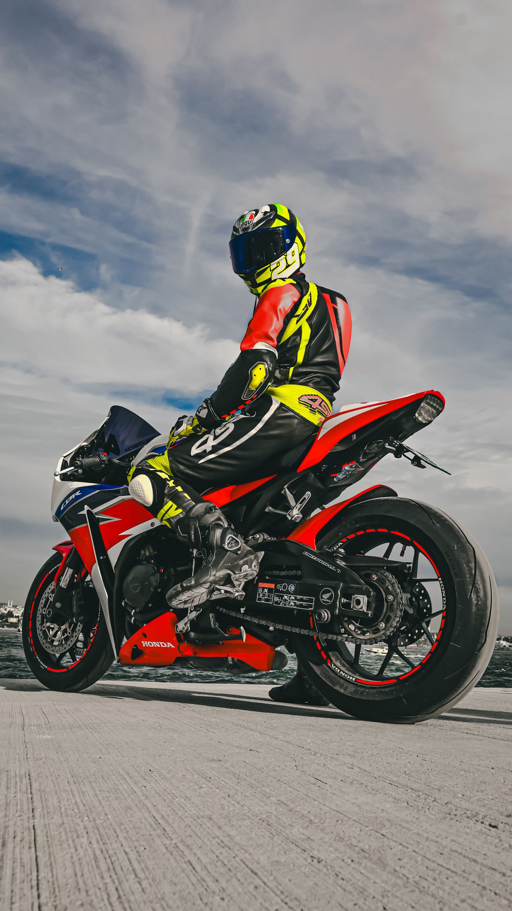 Biker in full gear on a parked Honda CBR1000RR Fireblade against a cloudy sky.