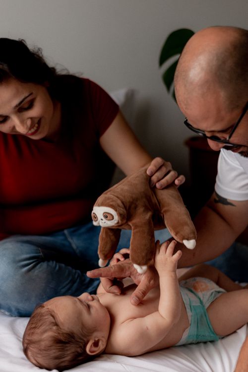 Free A happy couple plays with their baby using a toy sloth, capturing a joyful family bonding moment. Stock Photo