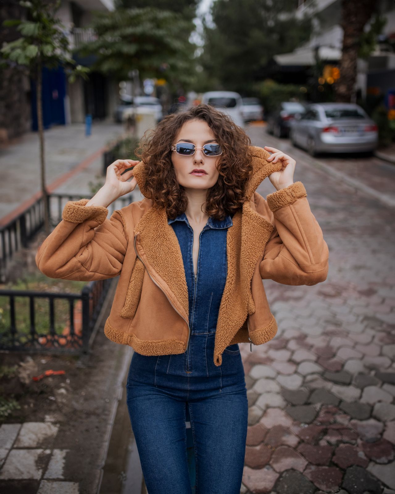 Woman wearing a camel shearling-trim suede jacket over a denim jumpsuit on a city street