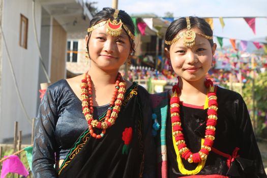 Two women in traditional attire with ornate jewelry at an outdoor celebration. Bright and colorful setting.