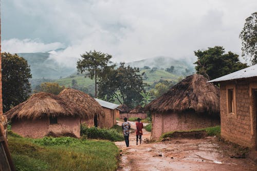 Two people walking down a dirt road in front of thatched huts