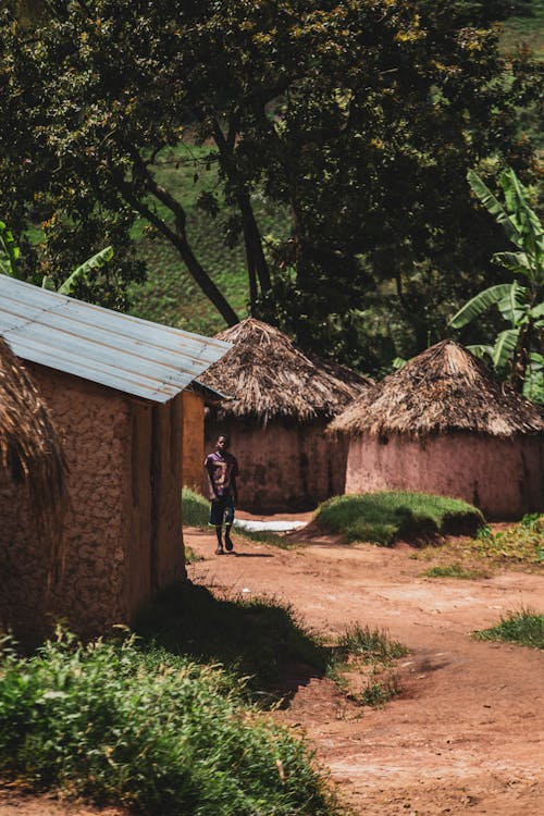 A man walks down a dirt road with thatched huts