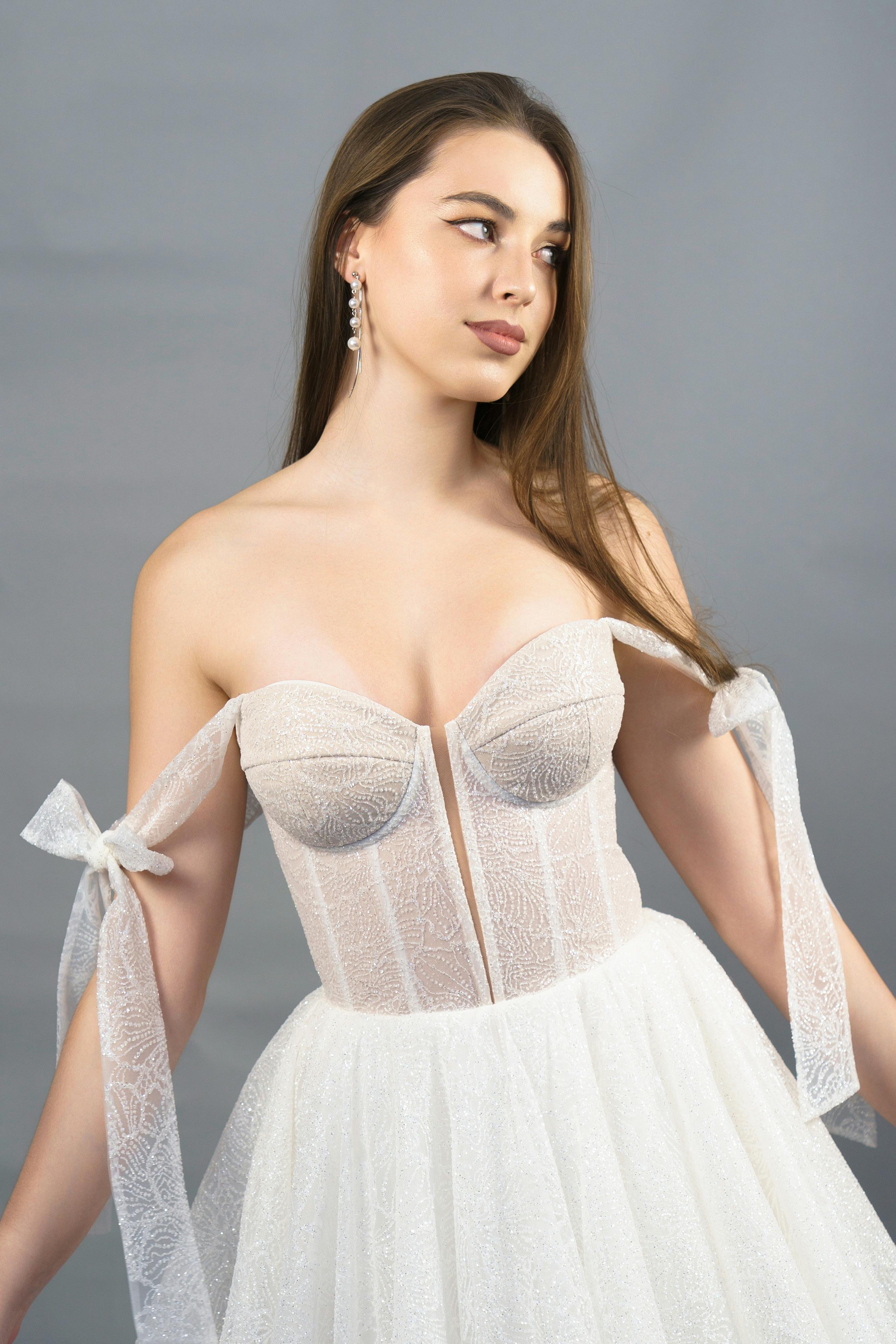 Elegant woman in a strapless wedding dress with gray background, studio shoot.