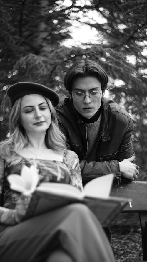 A man and woman sitting on a bench reading a book