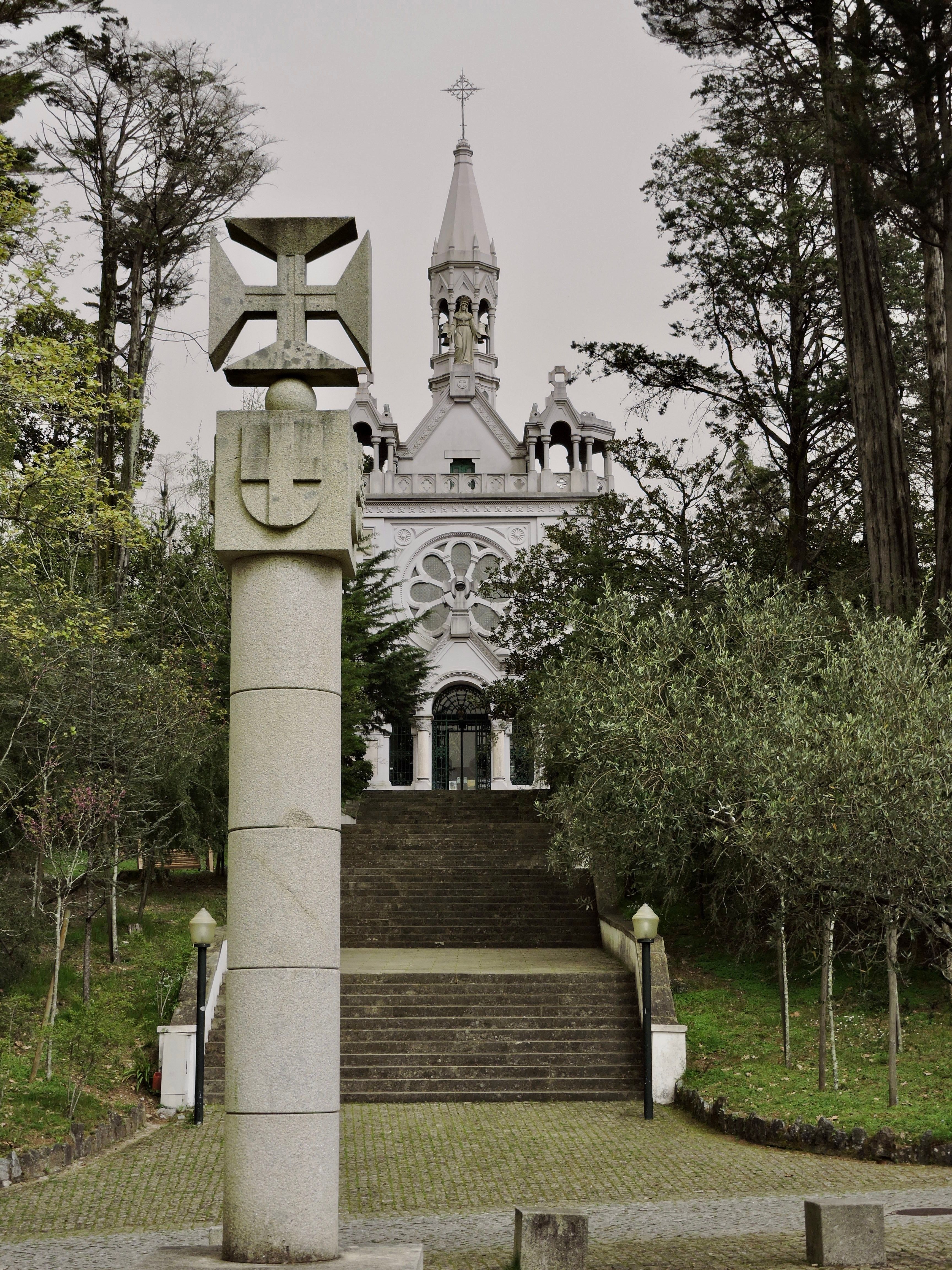 Stone cross and chapel in De La Salette Park, Oliveira de Azemeis, Portugal, surrounded by trees.