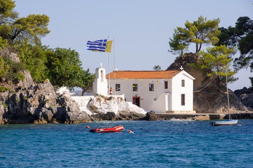 A church on a rocky island with a greek flag